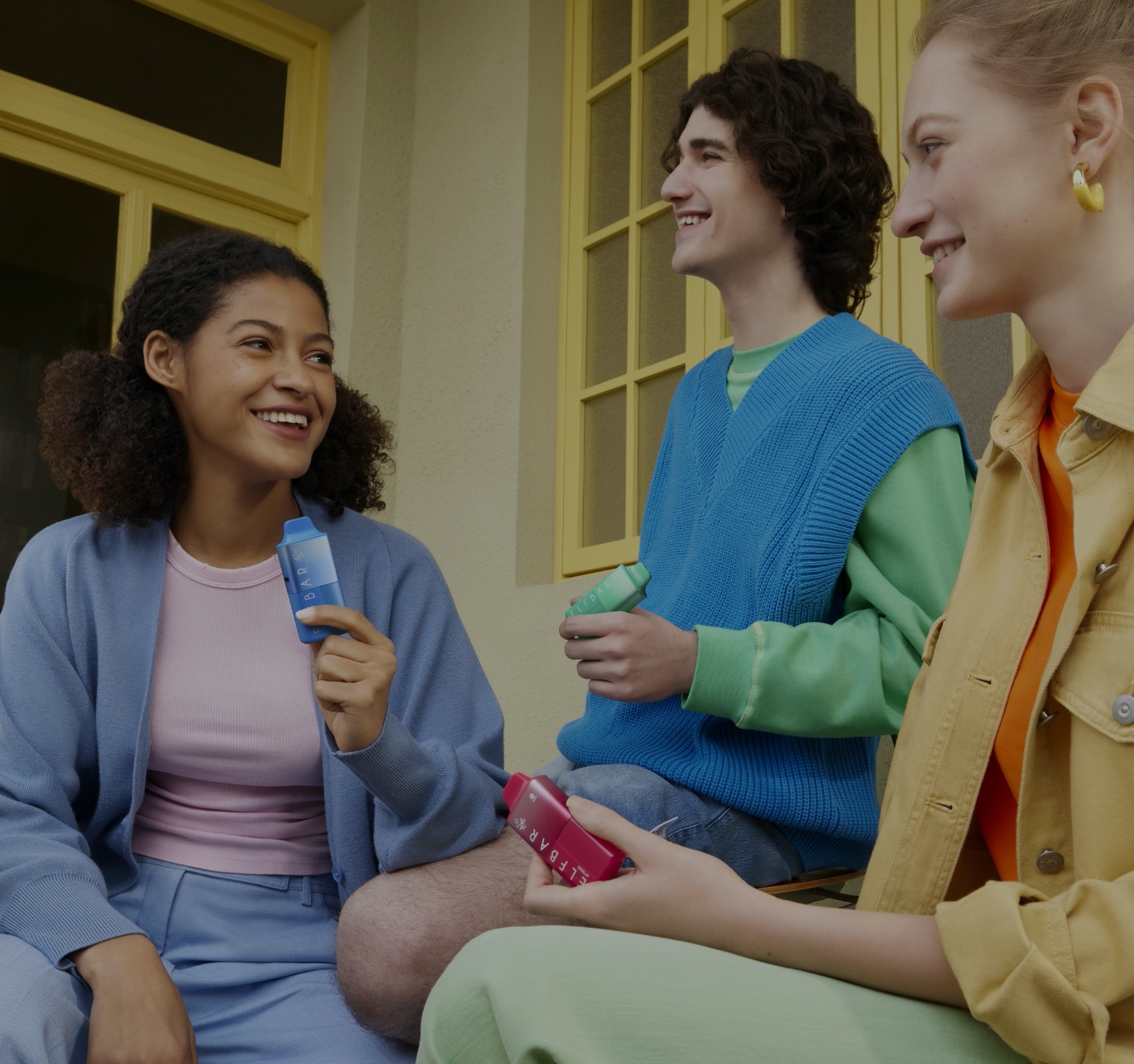 Three friends laughing together outside, each holding a device